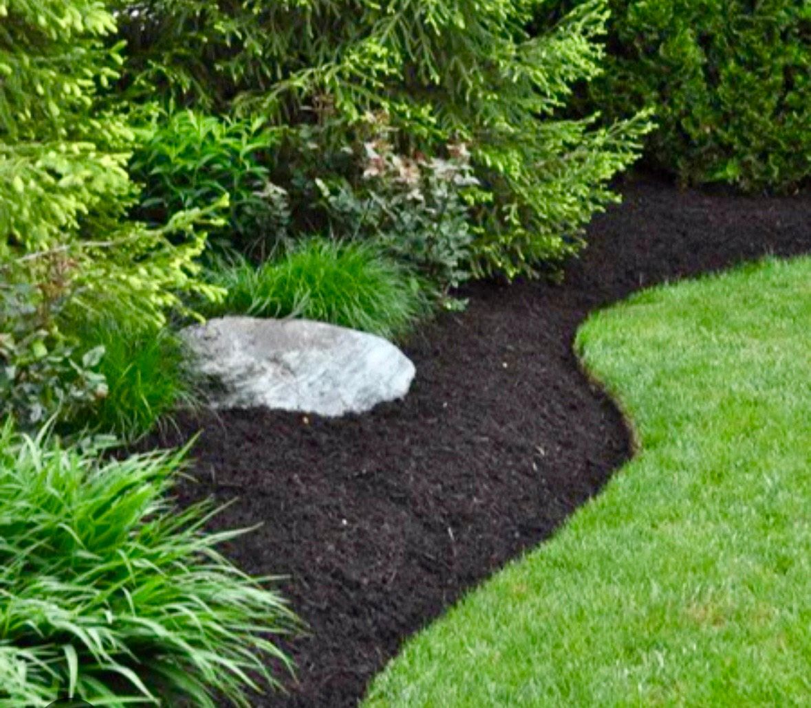 A person spreading mulch in a garden bed next to a light blue house.