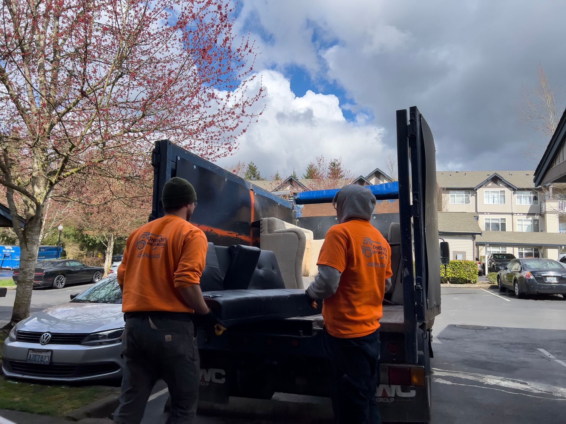 Two men are loading a couch into a dumpster.