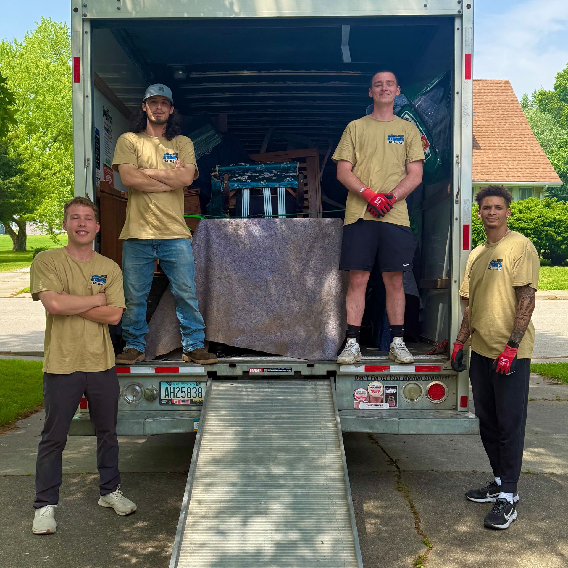 Two movers load a chair into a truck filled with boxes; house in the background.