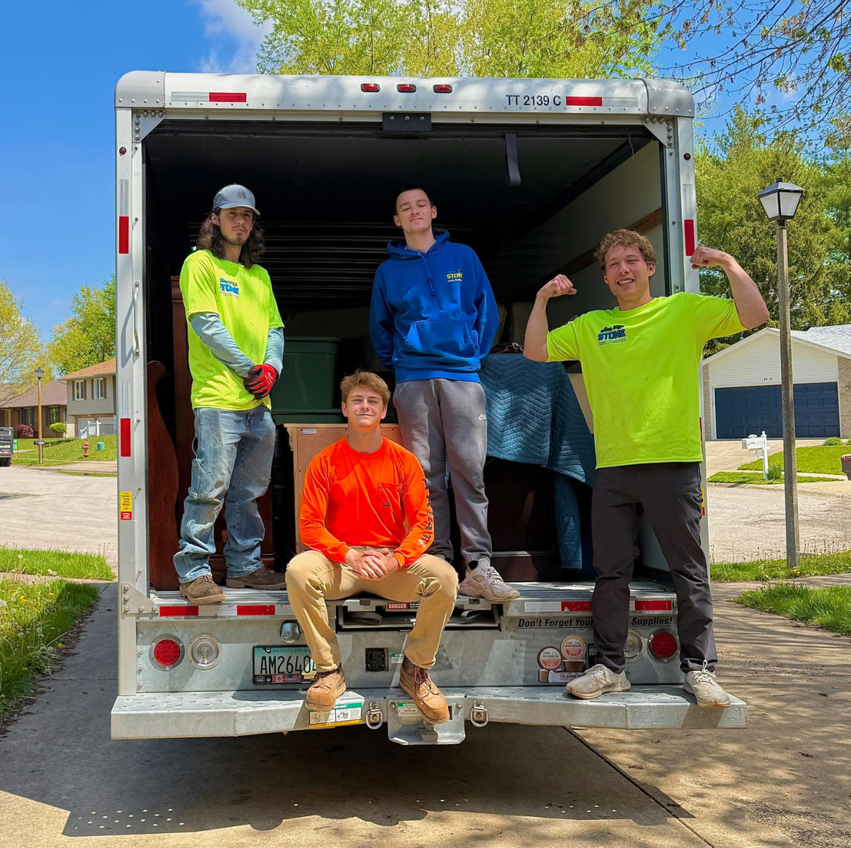 Two movers packing boxes in a bright room; one smiles while placing a plant, the other tapes a box.
