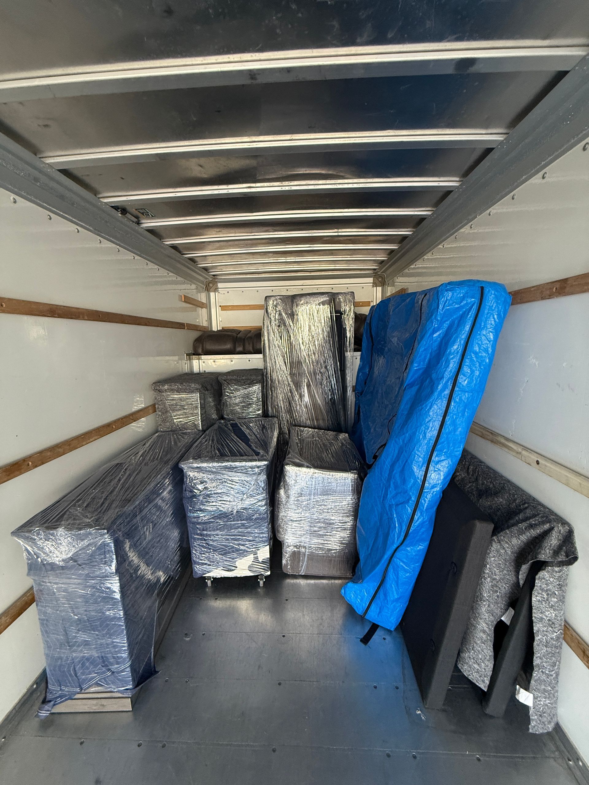 Office being packed for a move, with wrapped furniture, boxes, and a large window.