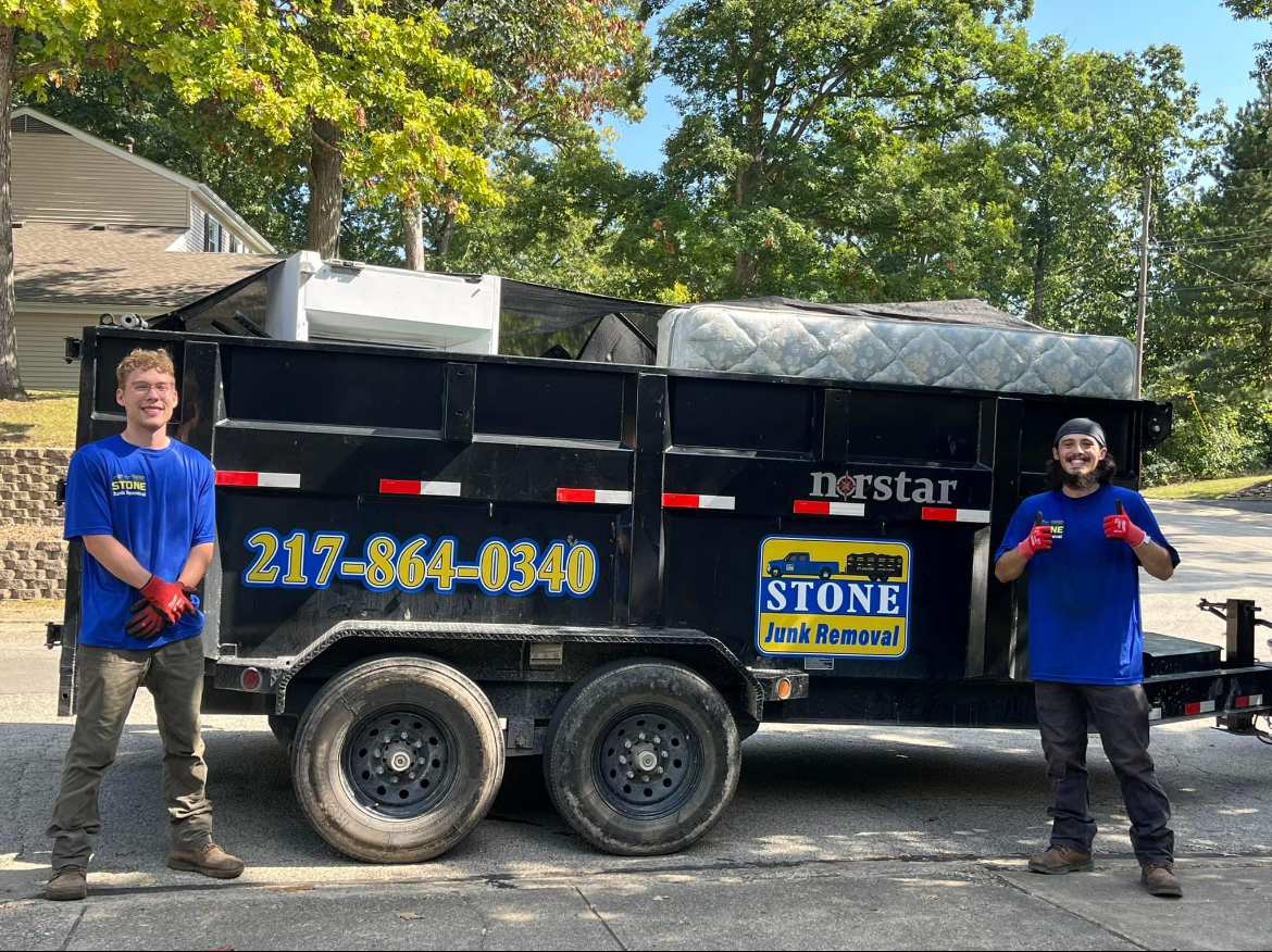 Two men are standing in front of a dumpster trailer.