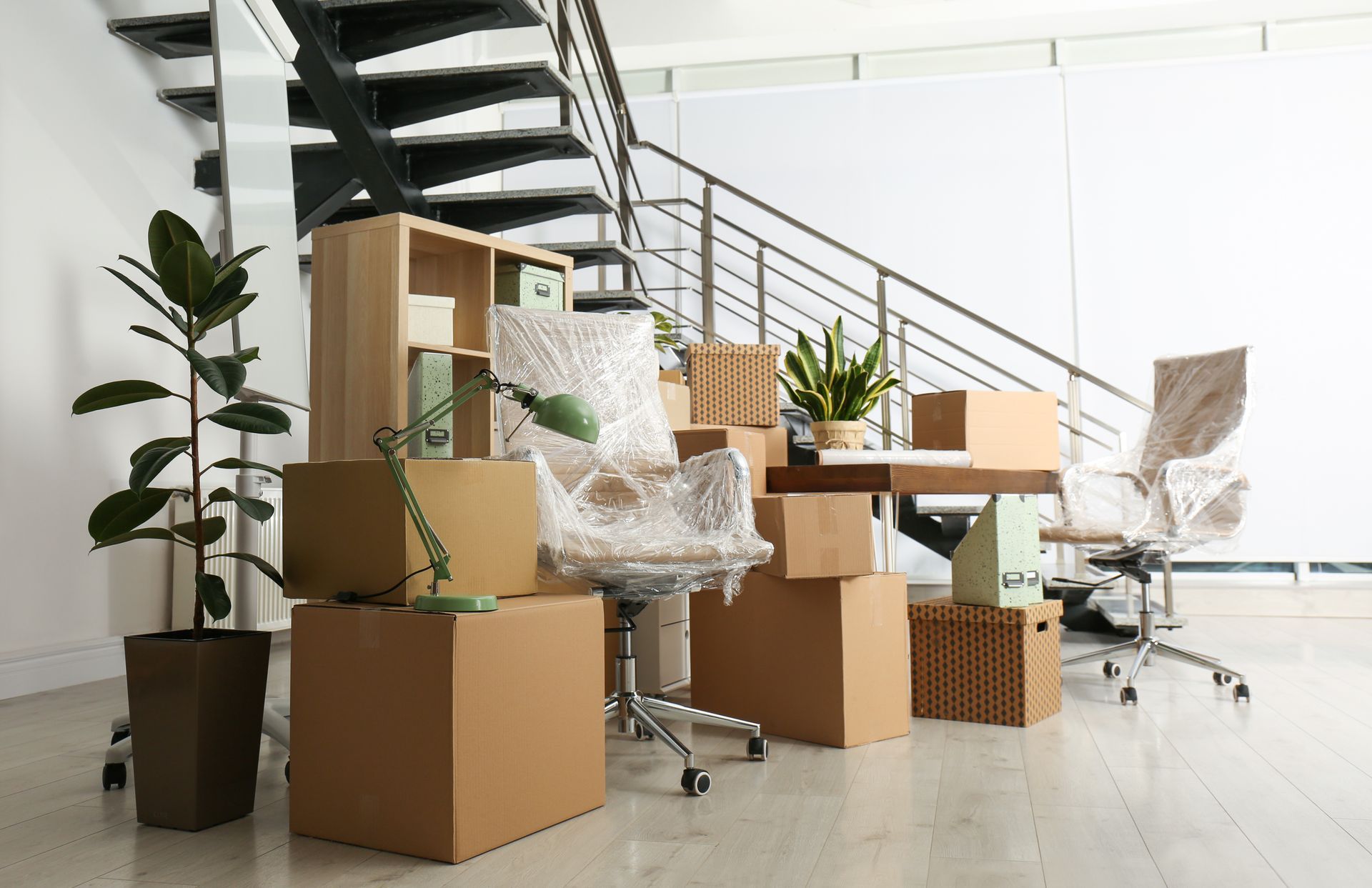 Office interior with packed boxes, furniture, and a staircase, indicating a move.