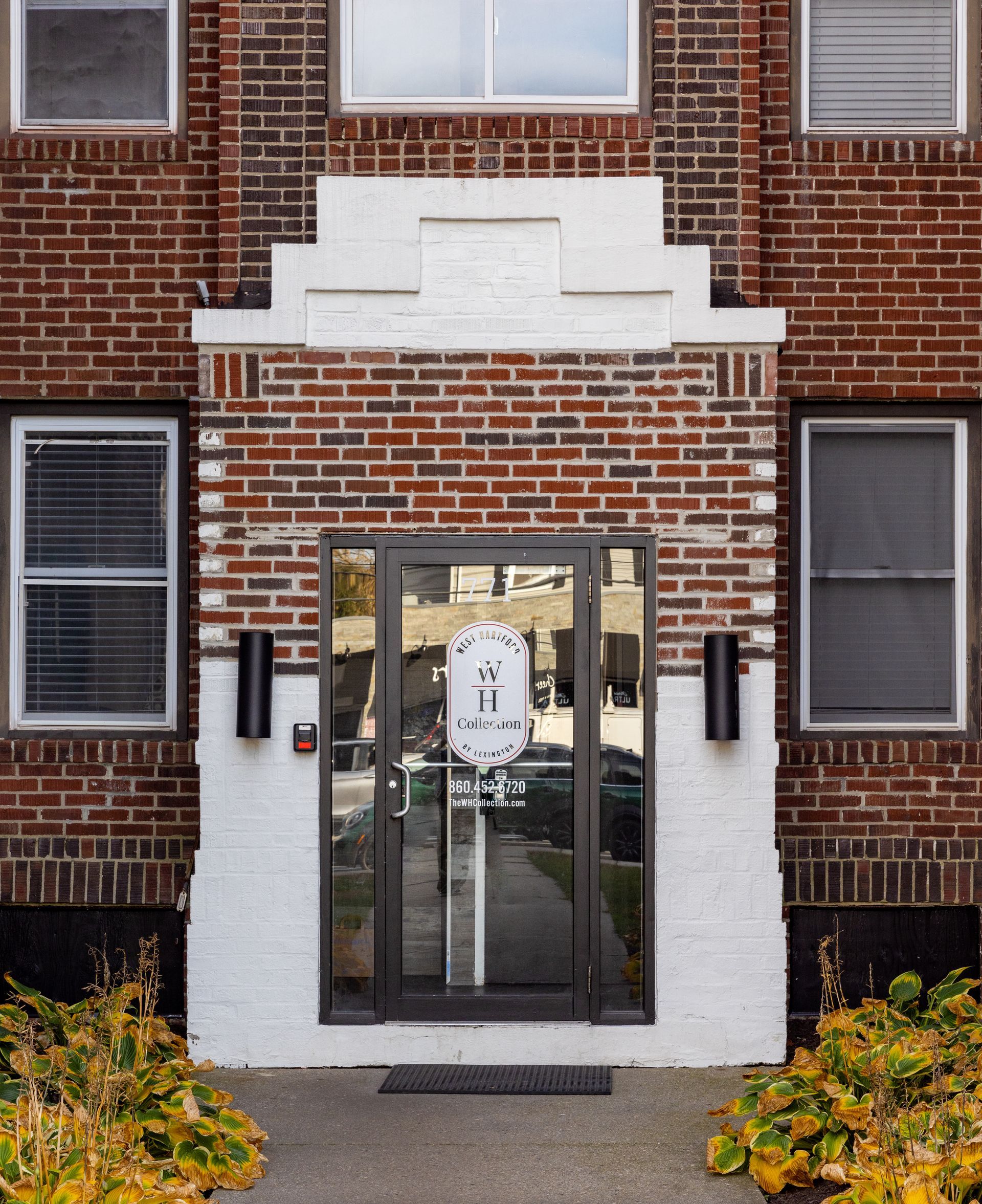 Brick building entrance with white trim, a glass door, and two black wall sconces.