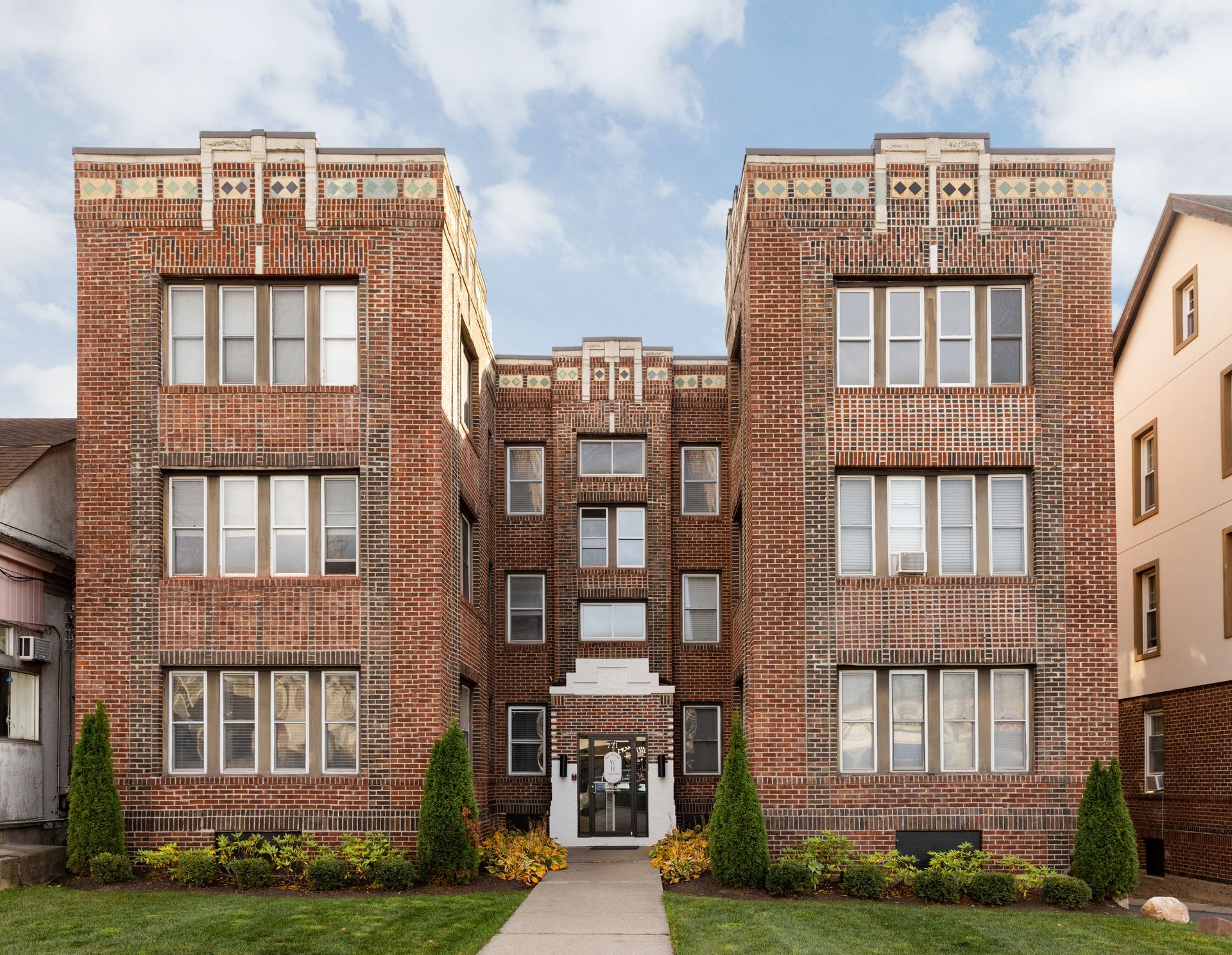Brick apartment building with symmetrical design, arched entrance, and small lawn.