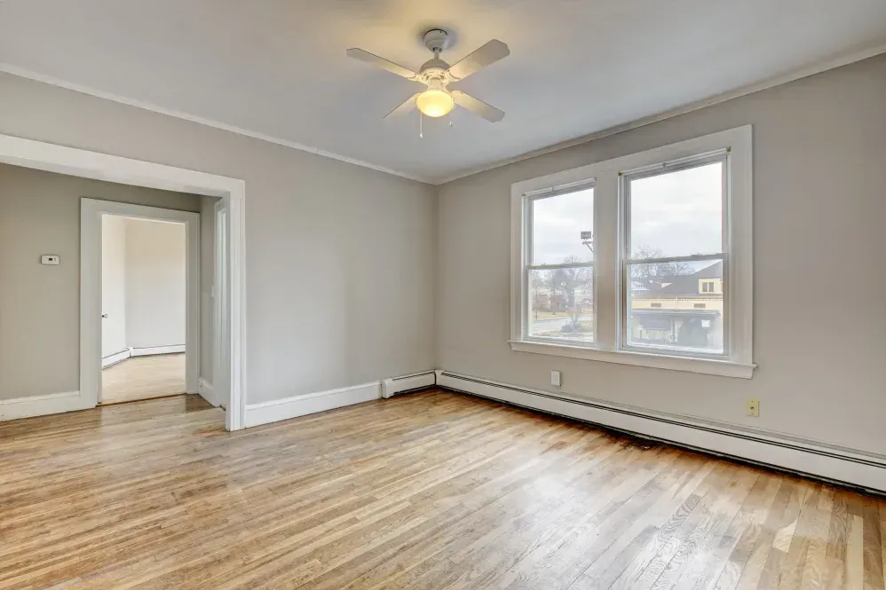 Empty room with hardwood floor, two windows, ceiling fan, and doorway.