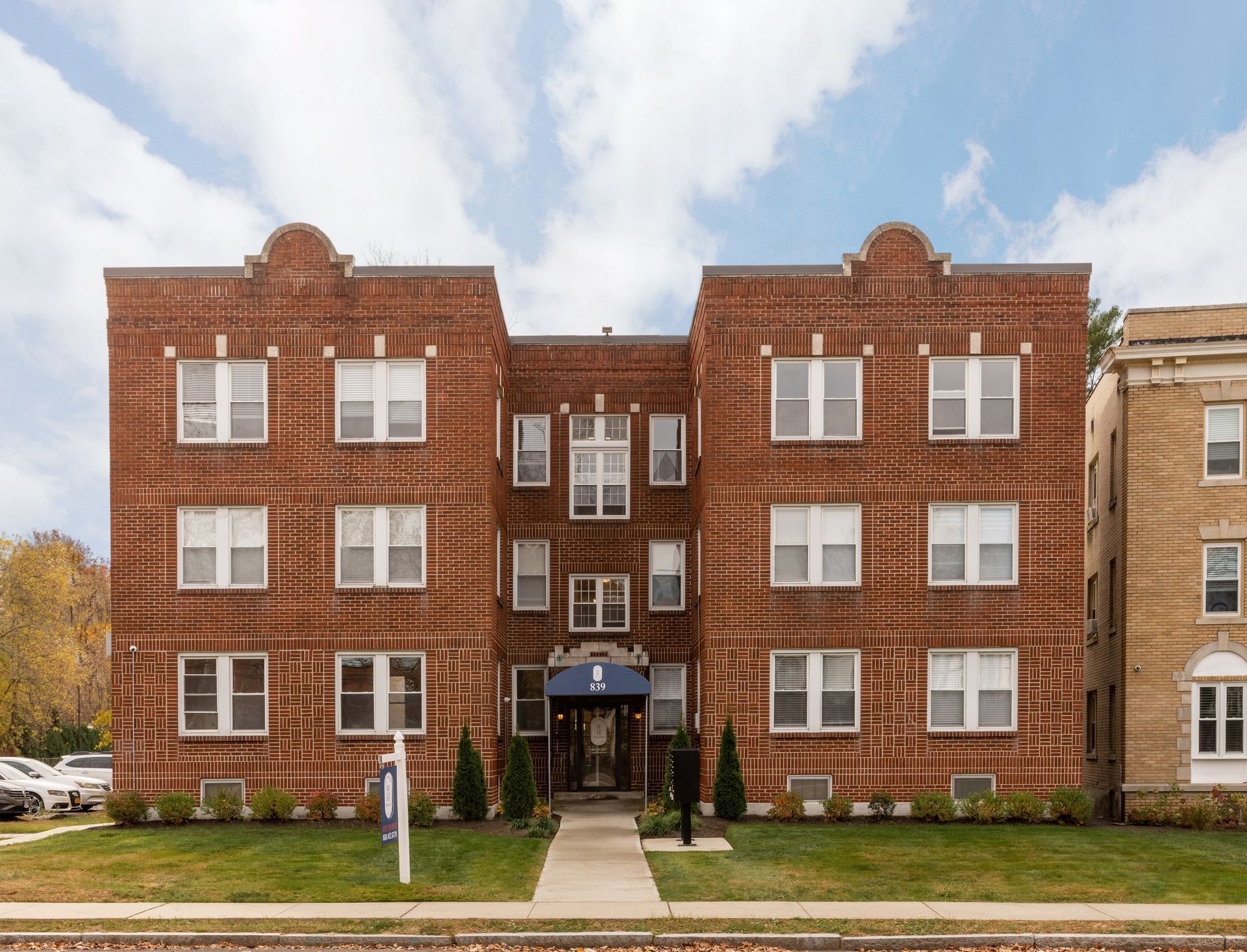 Red brick apartment building with white windows and blue awning over entrance.