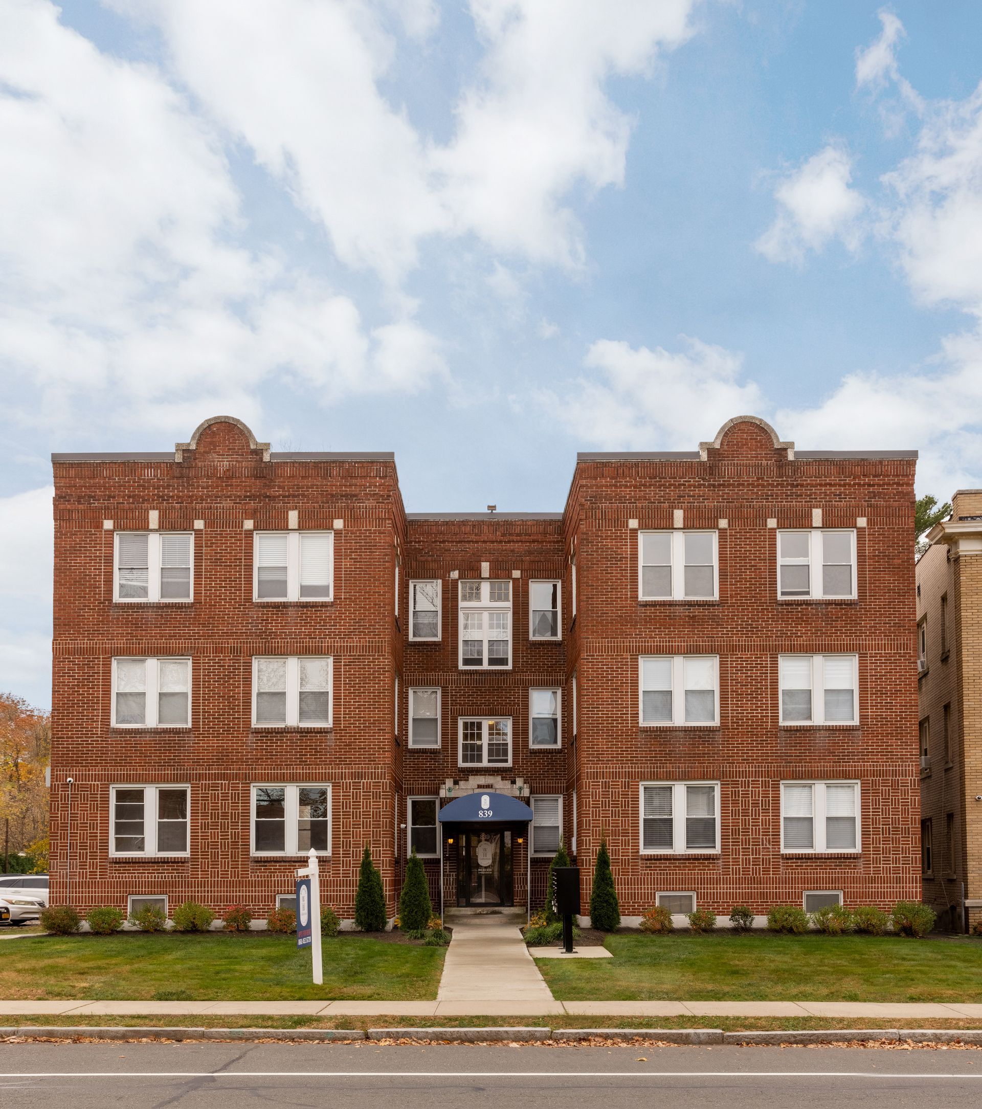 Red brick apartment building with a blue awning over the entrance, under a cloudy sky.