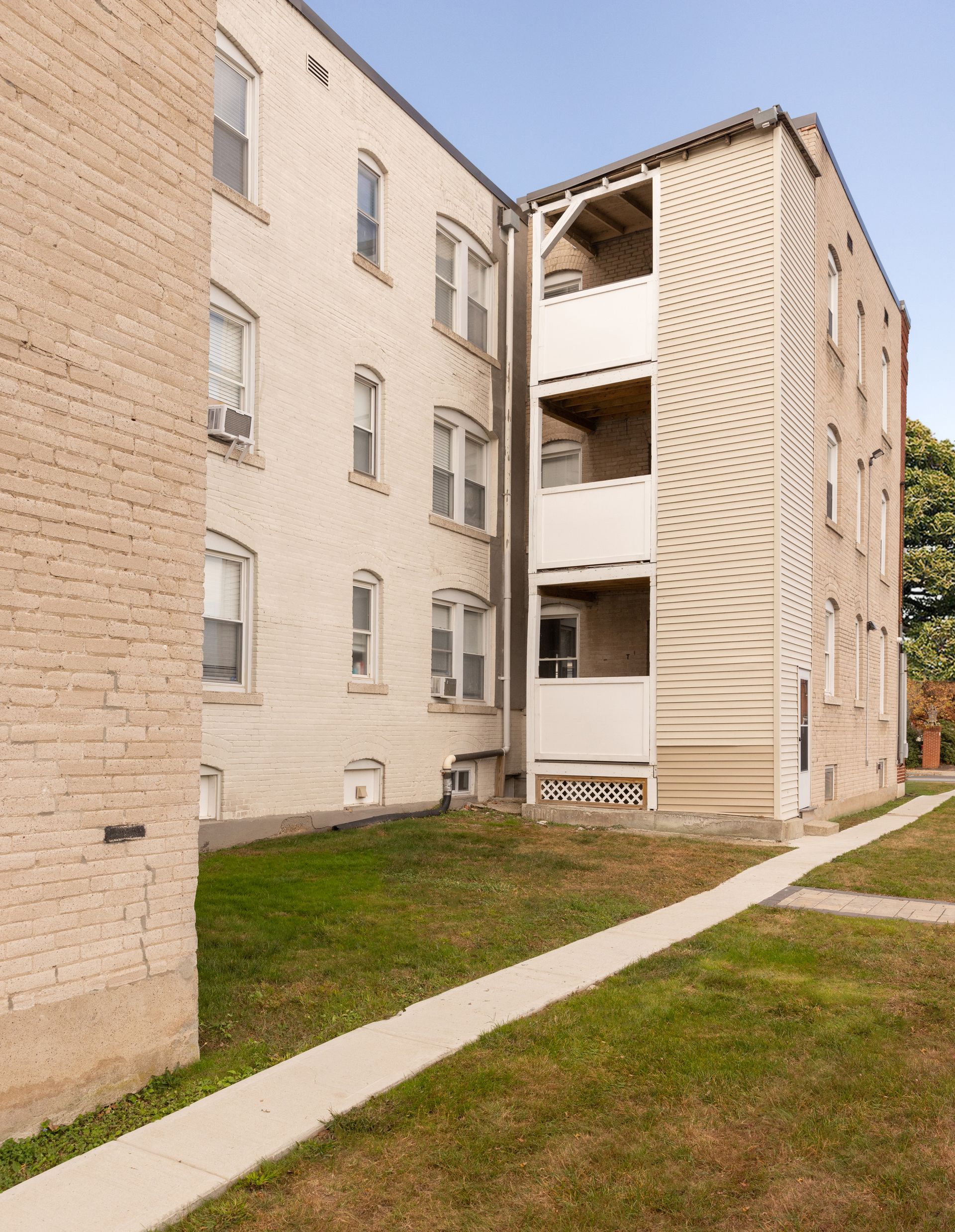 Exterior of a three-story brick apartment building with a walkway and small lawn.