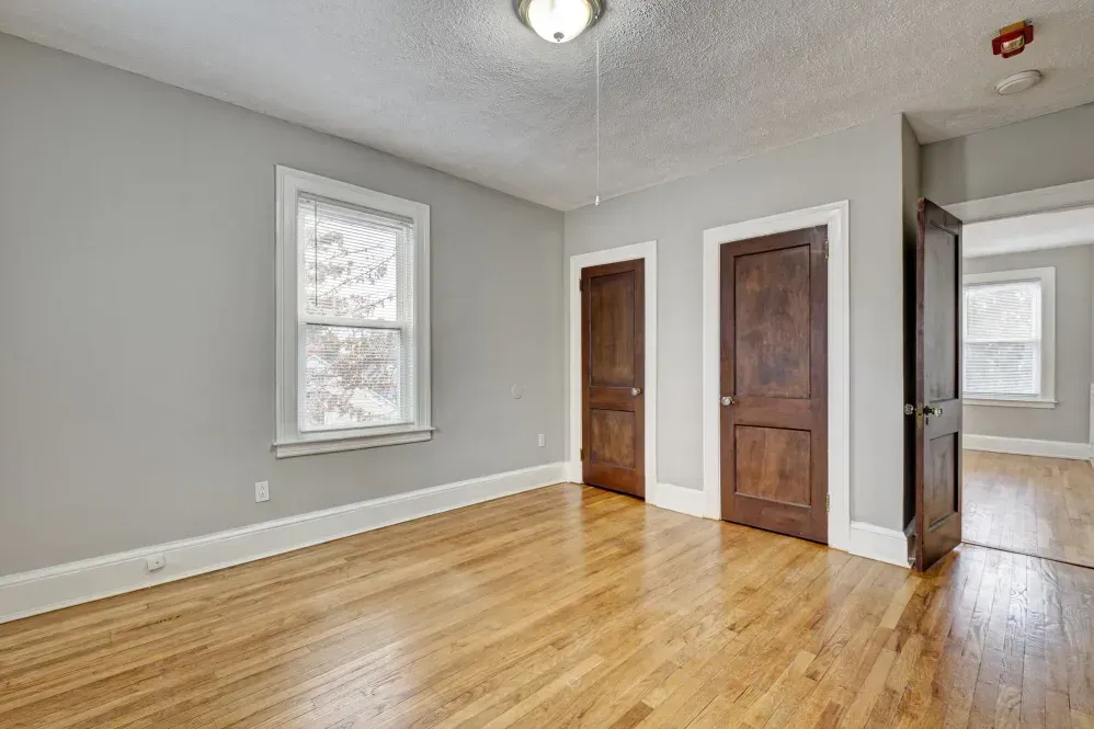 Empty room with light gray walls, wood floors, and dark wood doors and trim.