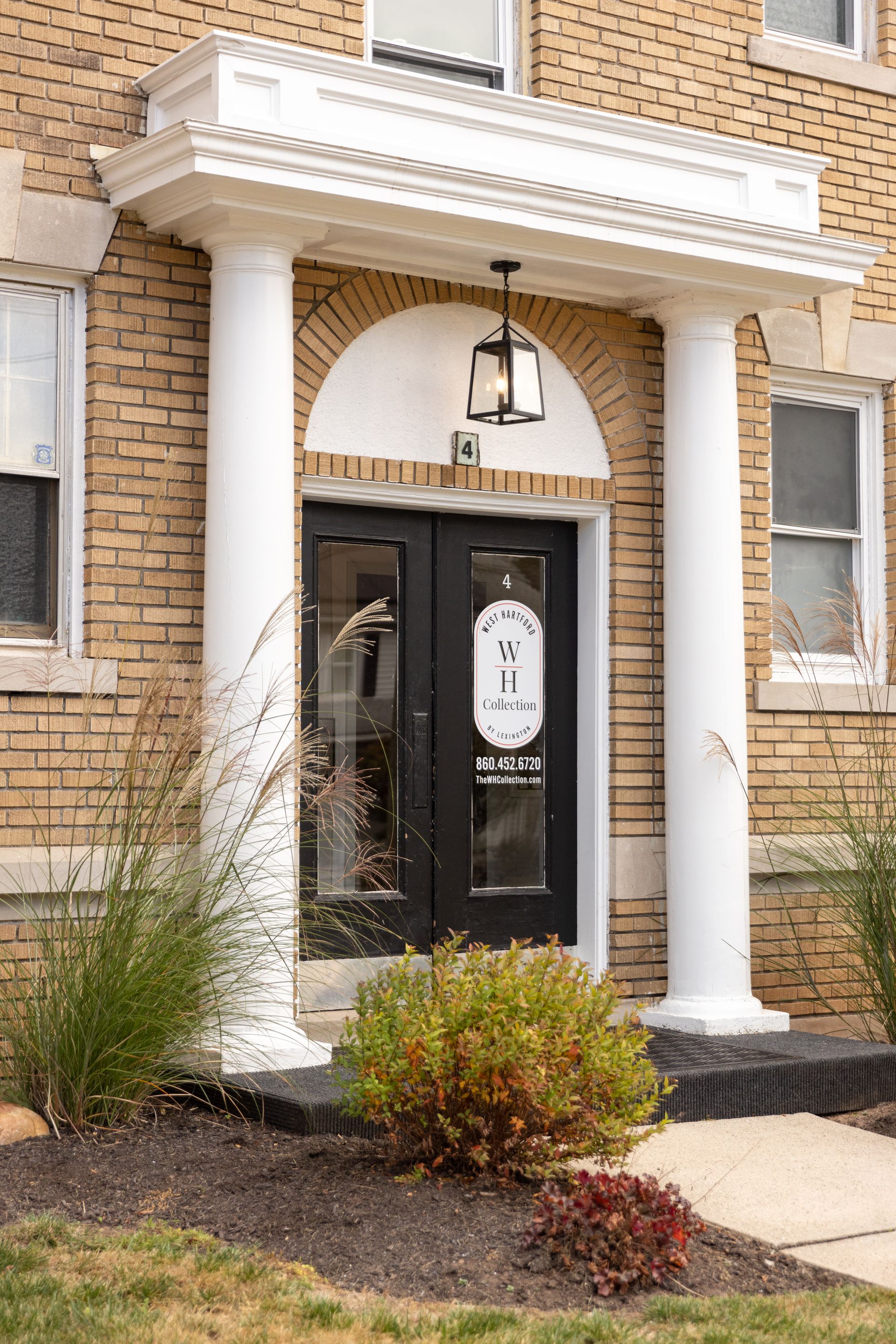 Building entrance with black double doors, white columns, and a decorative overhead canopy.