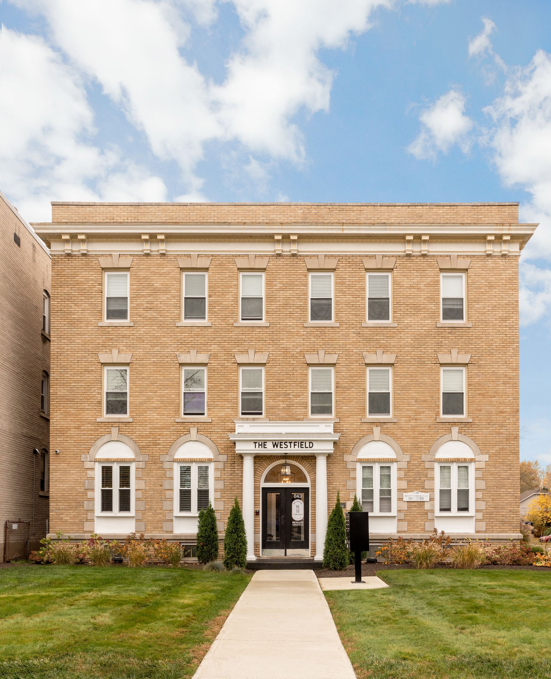 Three-story brick building with white trim and a walkway. Clear sky and green lawn.