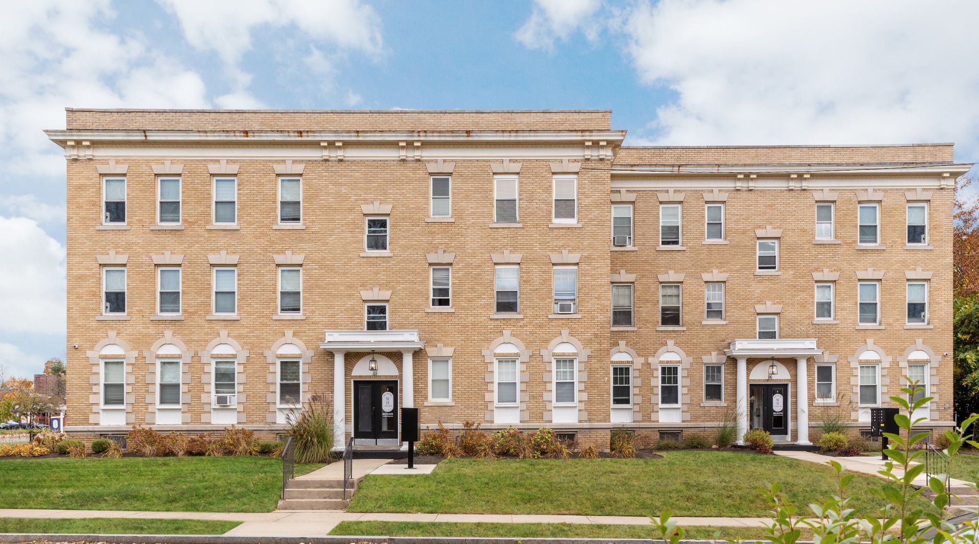 Beige brick apartment building with many windows and two entryways under a blue sky.