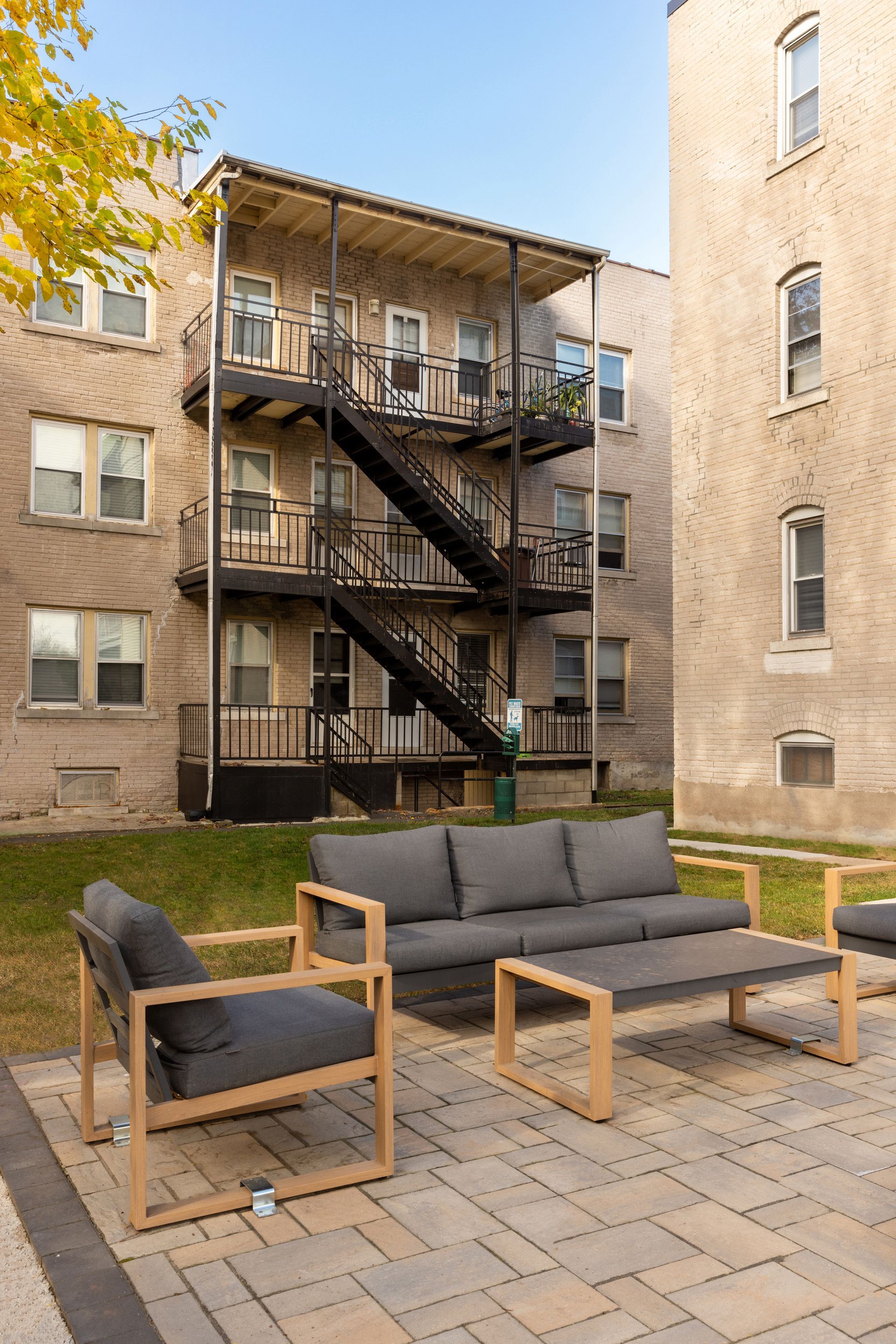 Outdoor seating area with gray furniture and brick buildings, a black fire escape.