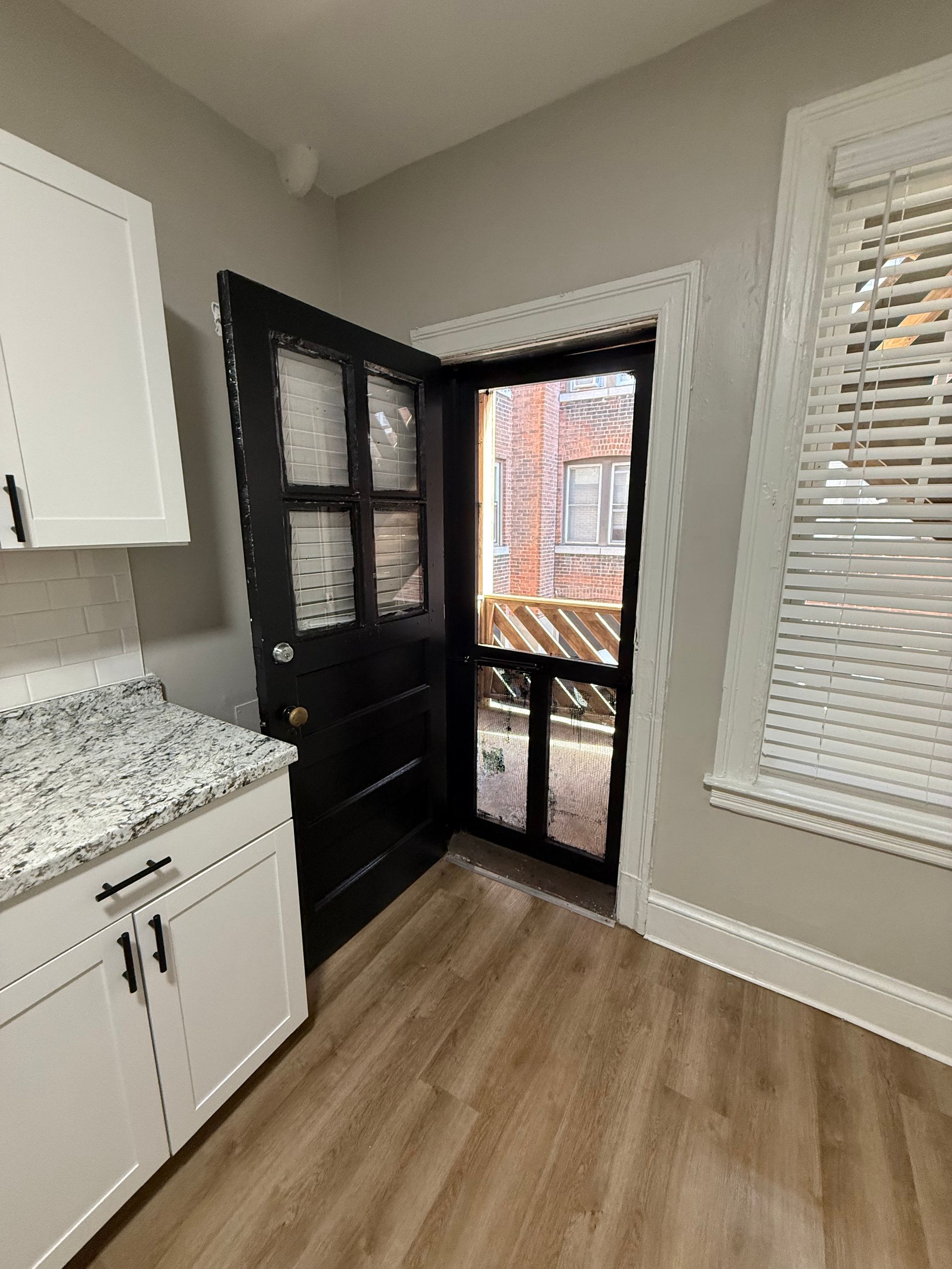 Renovated kitchen with white cabinets and a black door leading to an outdoor porch