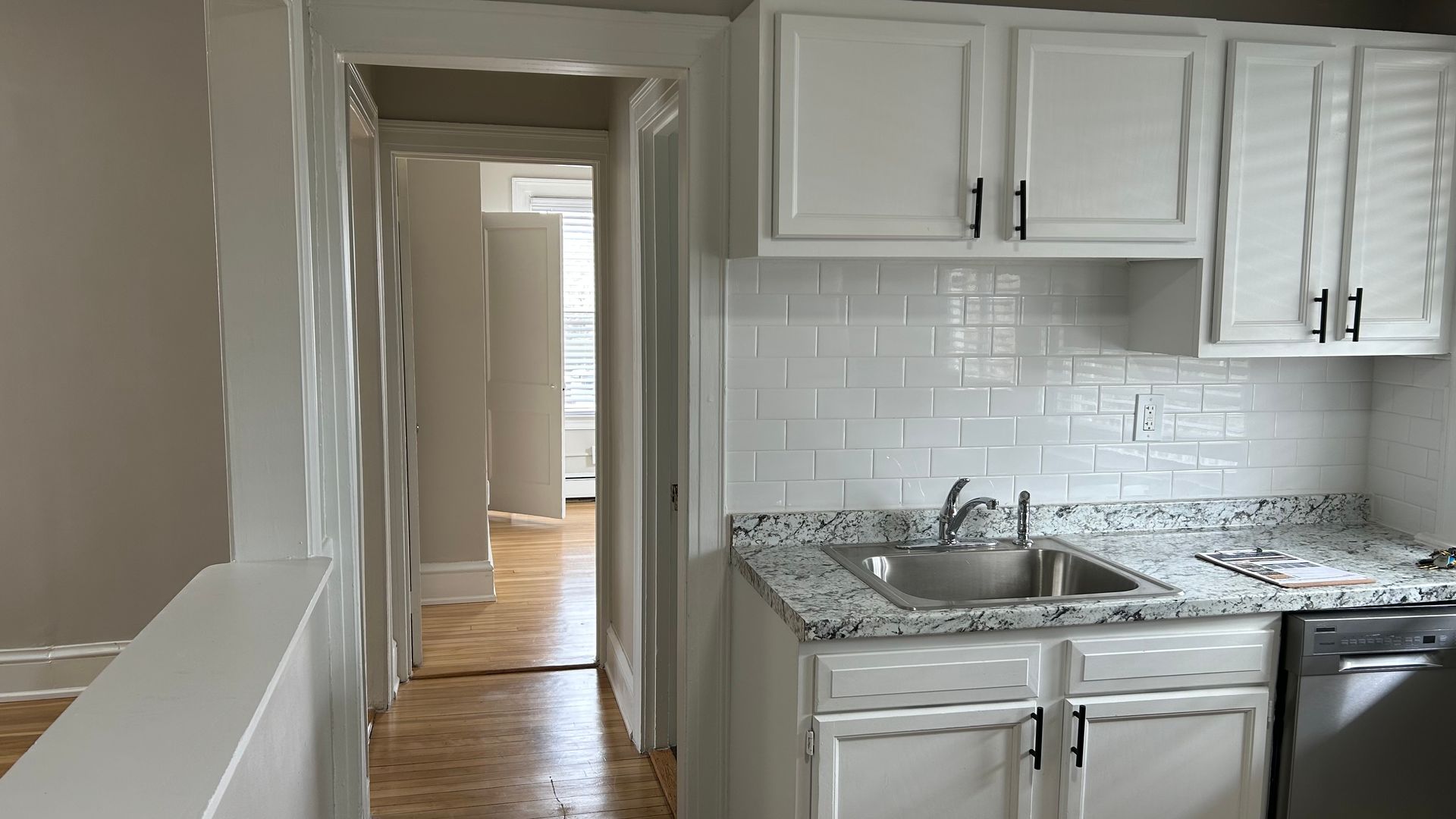 Renovated kitchen with white cabinets , hardwood flooring, and stainless steel appliances