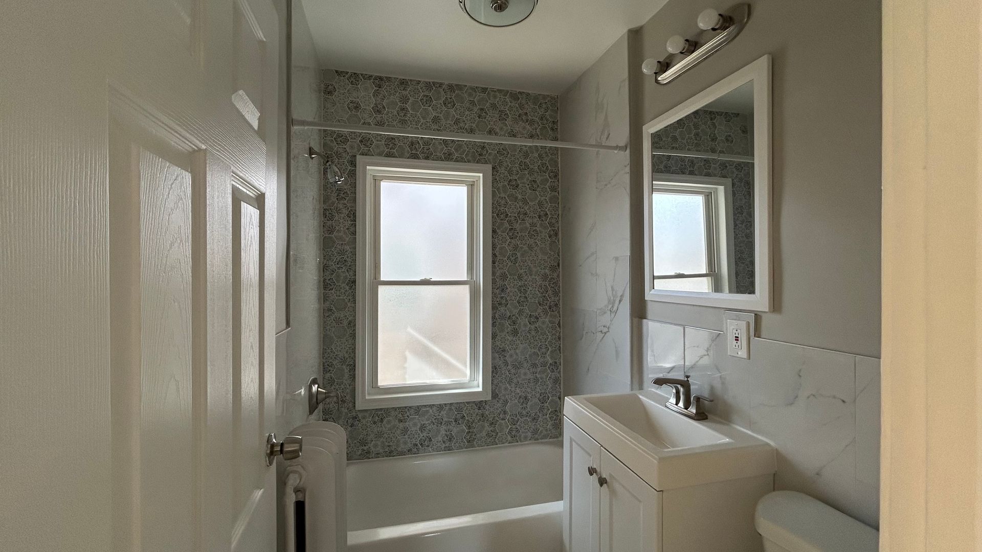 Renovated bathroom with a mirror, porcelain toilet, shower, and bath
