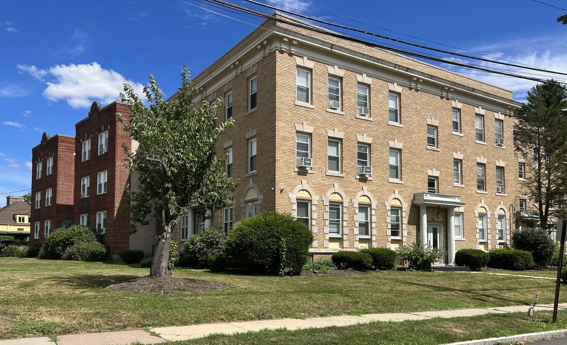Multi-story brick apartment buildings with a lawn in front, under a blue sky.