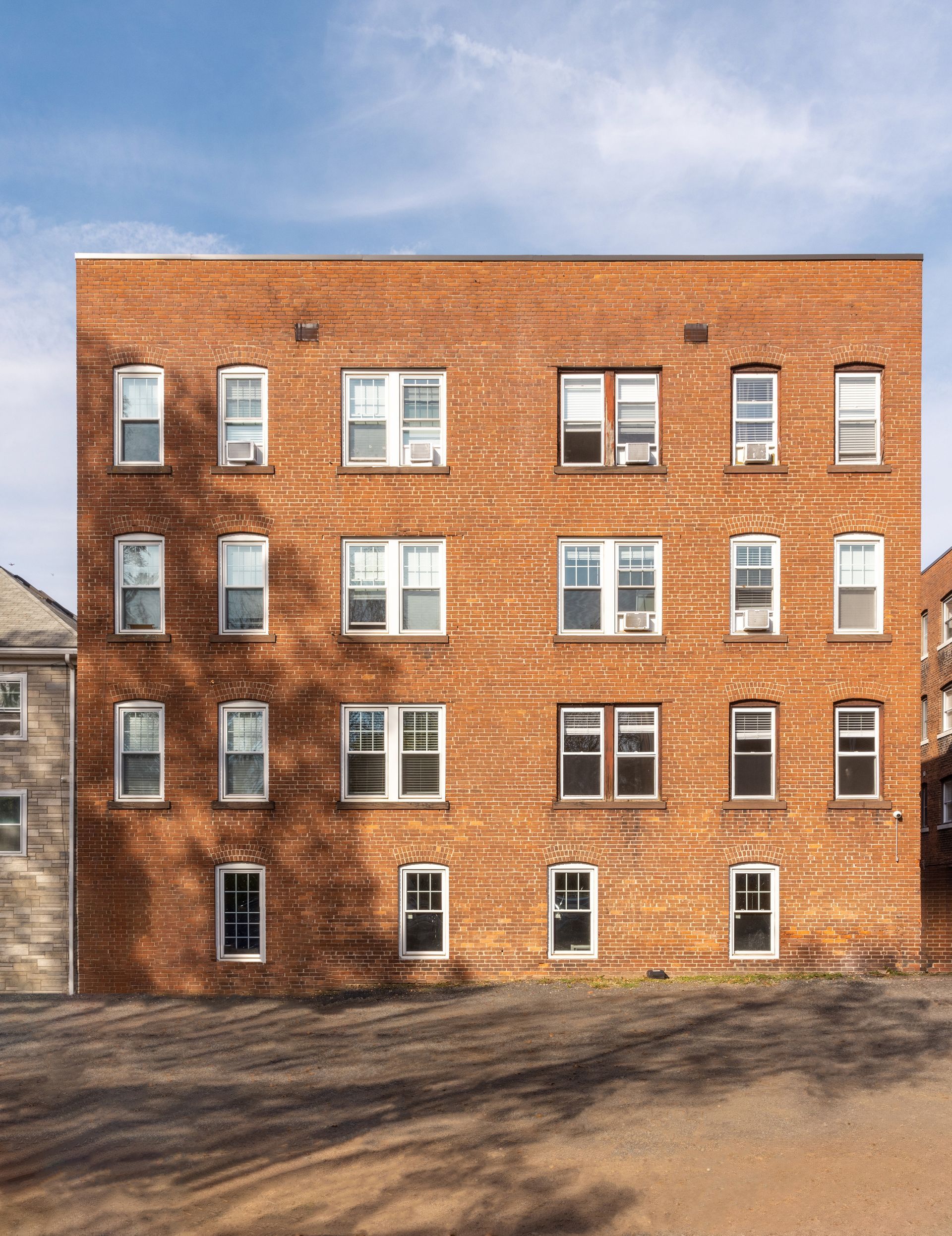 Red brick apartment building with multiple white-framed windows against a partly cloudy blue sky.
