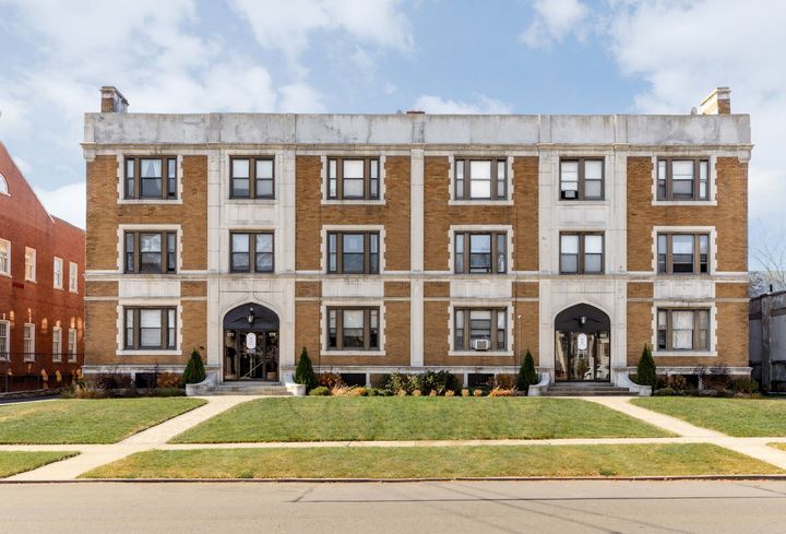 Two-story brick apartment building with white trim and archway entrances, set on a grassy lawn.