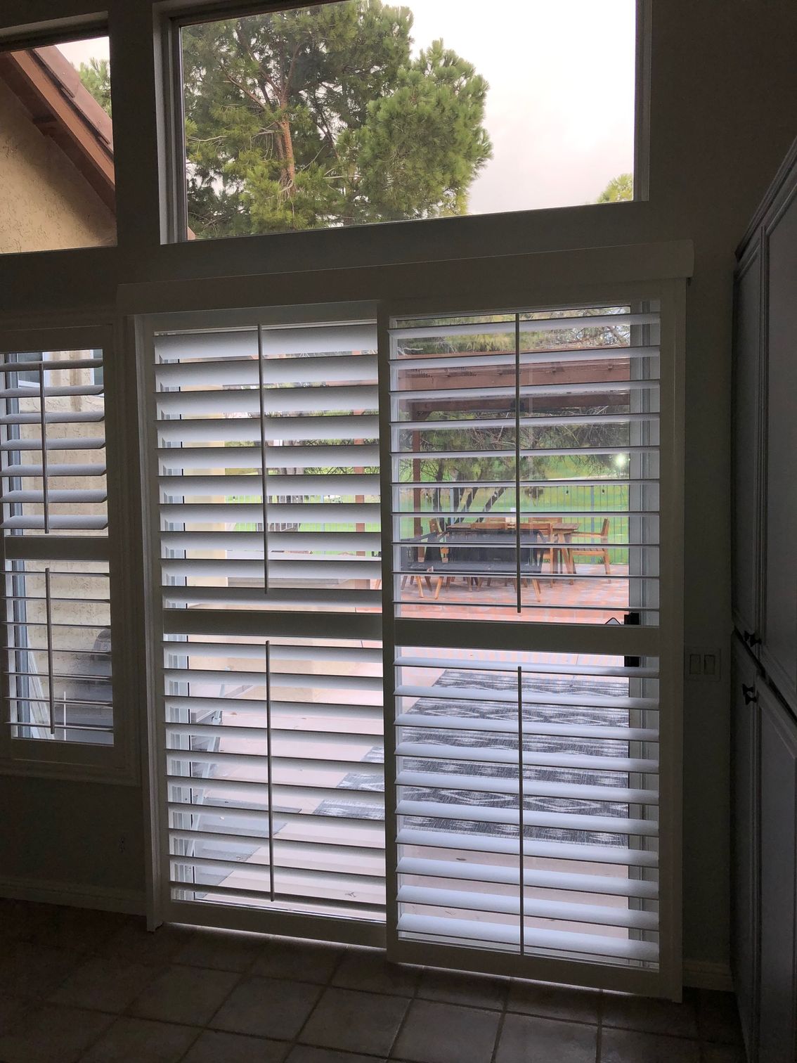 A room with a sliding glass door and shutters on the windows
