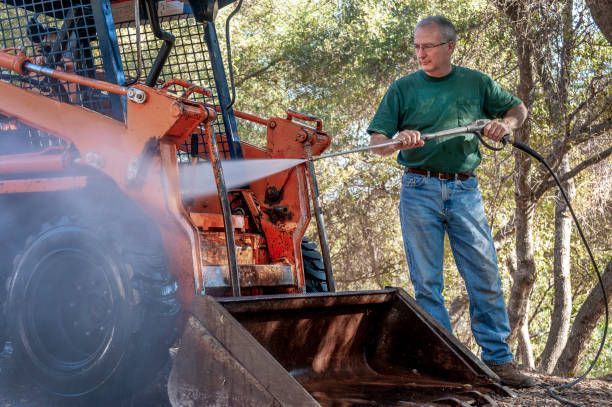 A man is cleaning a tractor with a high pressure washer.