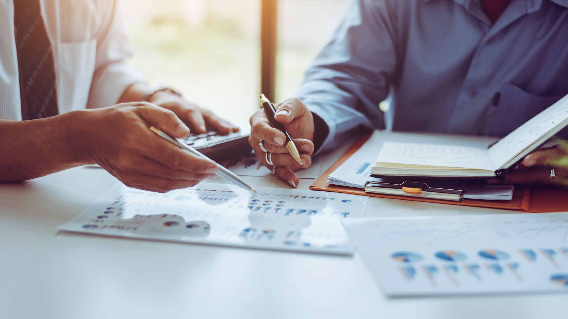 Two men are sitting at a table looking at papers and a calculator.