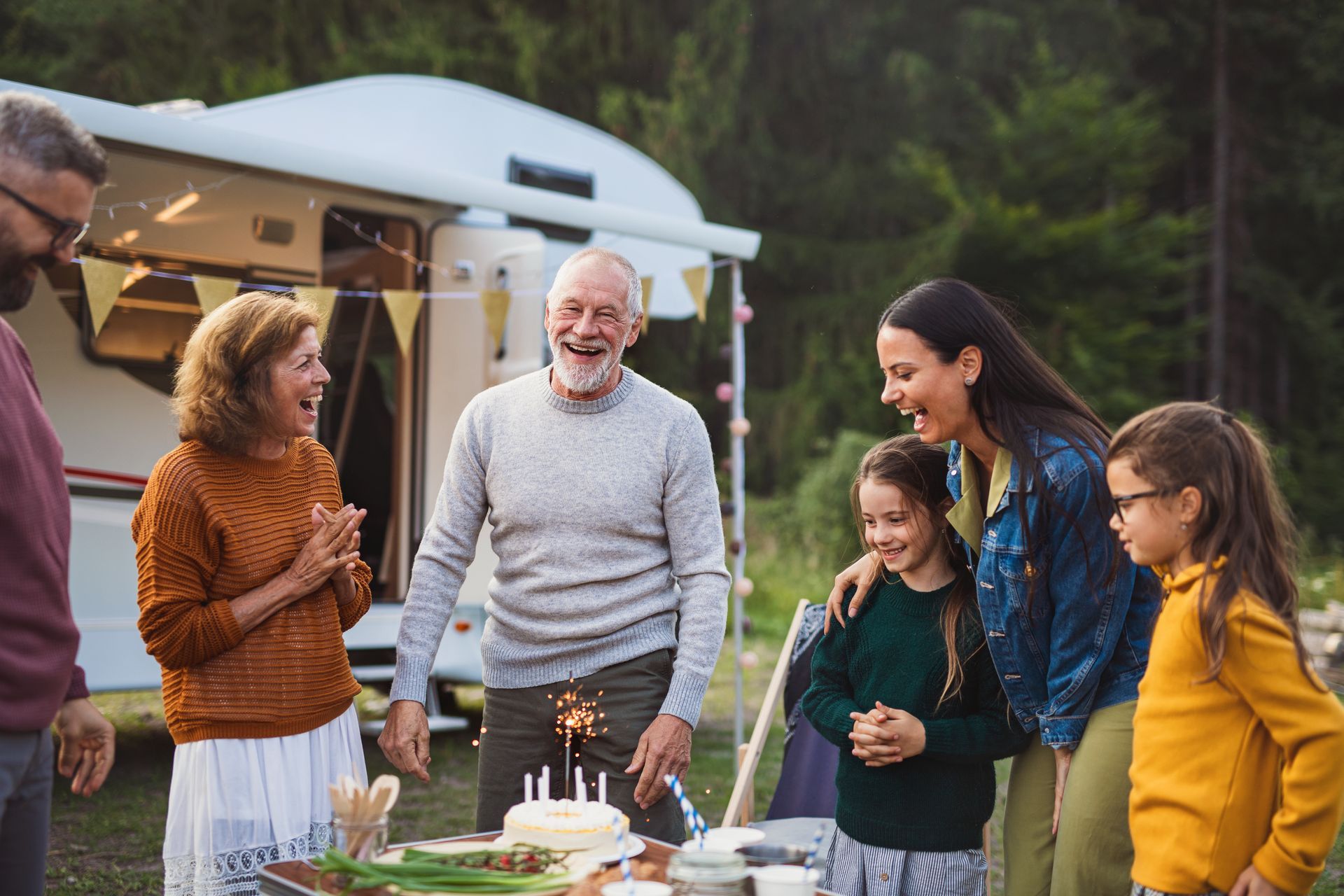 A family is celebrating a birthday in front of a trailer.