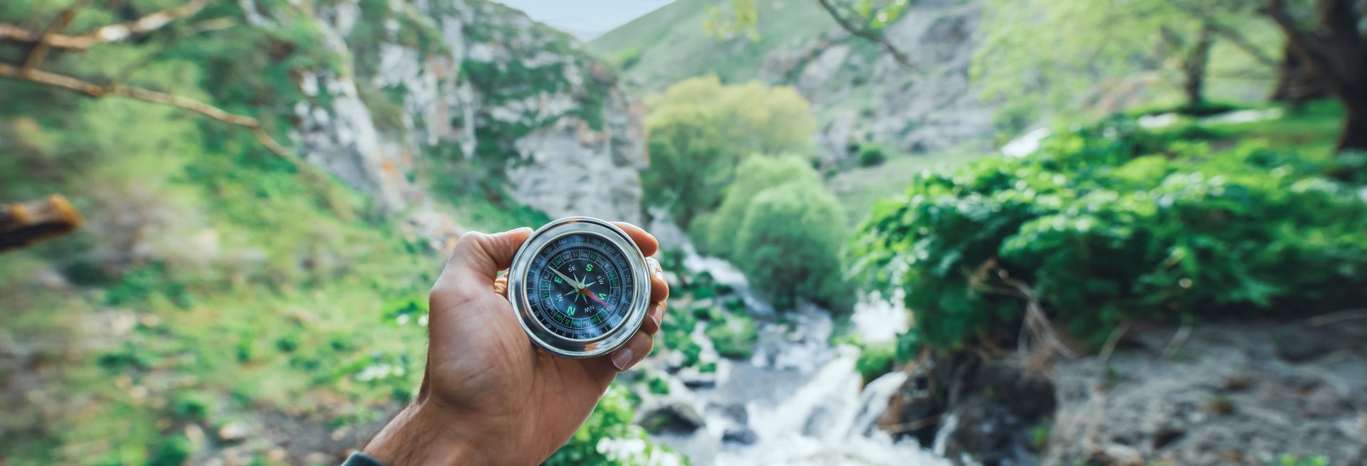 A person is holding a compass in front of a waterfall.