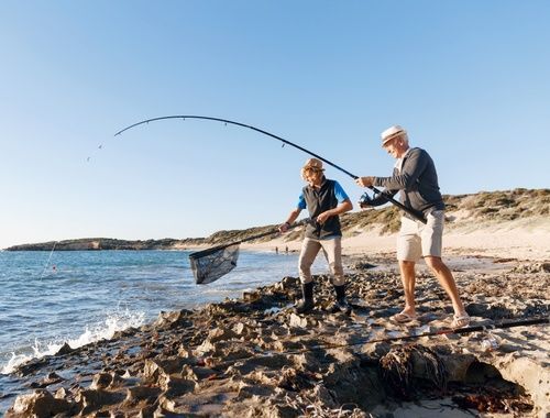 Two men are fishing on a rocky beach near the ocean.