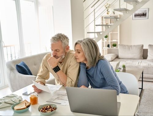A man and a woman are sitting at a table looking at a laptop.