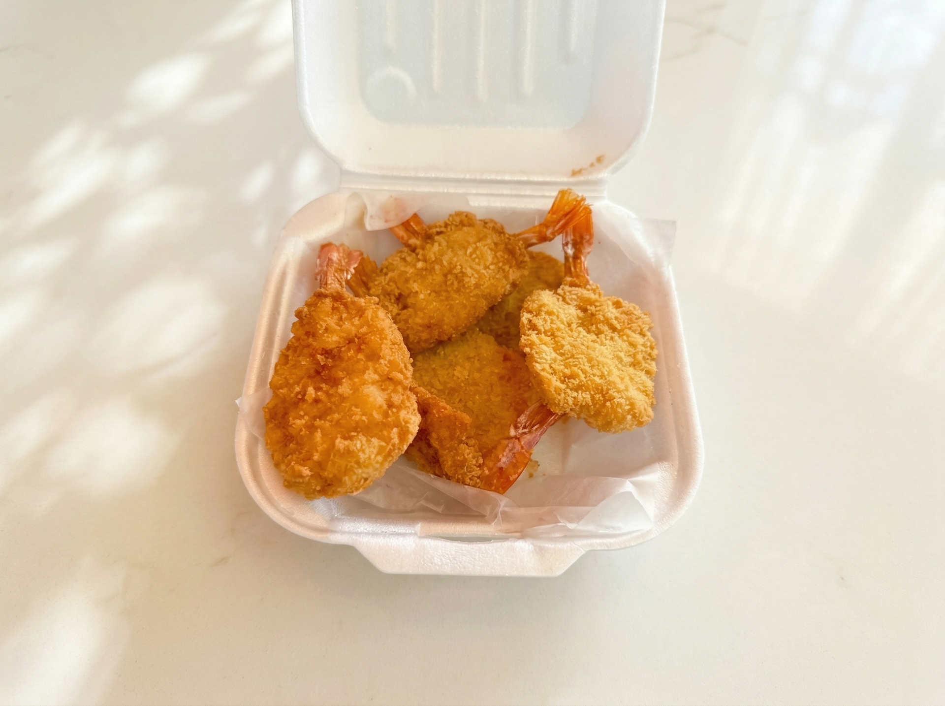 A white styrofoam takeout container filled with several breaded, deep-fried shrimp on white parchment paper.