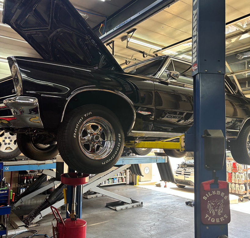 A black vintage car with its hood open, raised on a hydraulic lift inside an auto repair shop. | Waggener Brake and Auto Repair