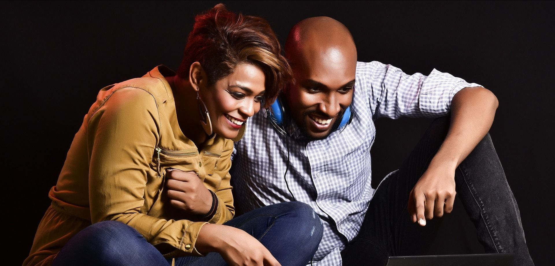 A man and a woman are sitting next to each other looking at a laptop.