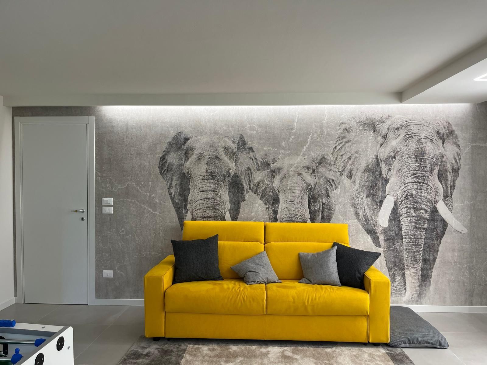 Un soggiorno con un divano giallo e un quadro di elefanti sulla parete.