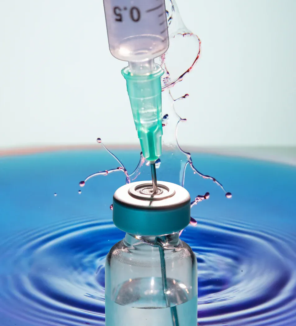 Syringe injecting liquid into a medicine vial, surrounded by blue water.