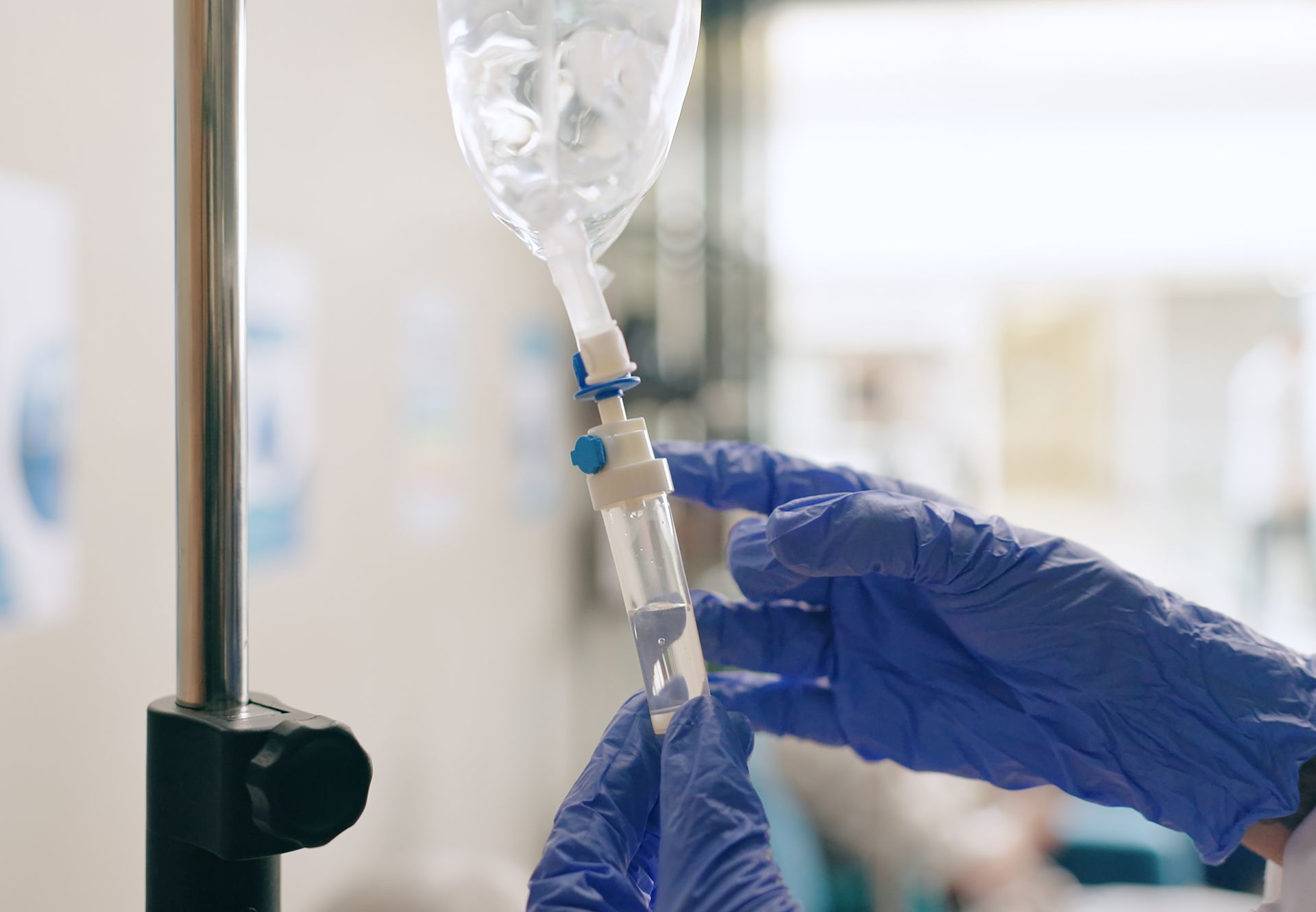 Gloved hands adjusting an IV drip in a hospital setting