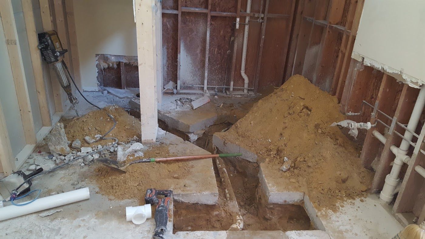 Bathroom under renovation: demolition debris, exposed framing, jackhammer, concrete blocks, and sand.