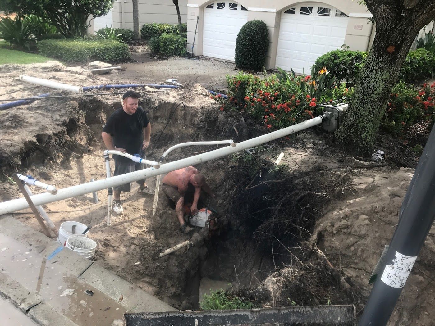 Men working in a large hole in front of a house, fixing pipes.