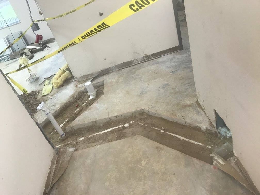 Hallway under construction, caution tape, exposed floor, plumbing, debris.