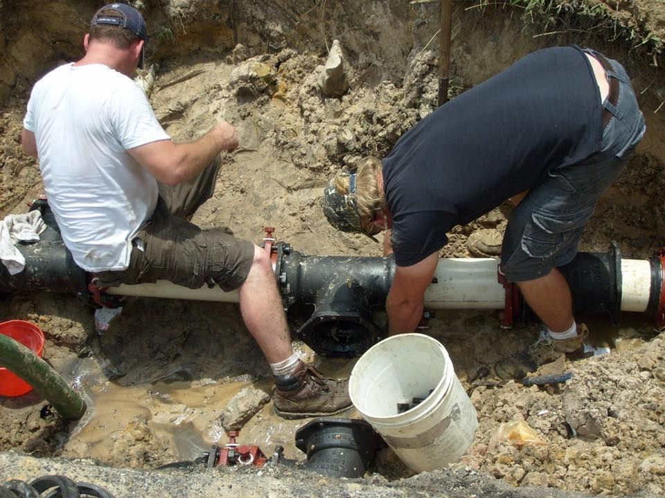 Two workers install a pipe underground; one in white, one in black, both in work boots.