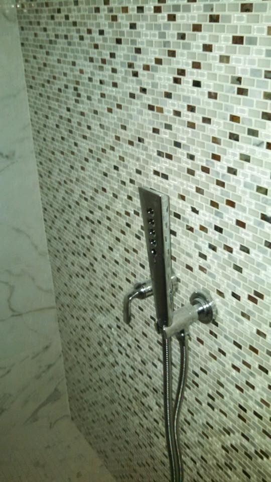 Showerhead and faucet on a mosaic tile wall in a bathroom.