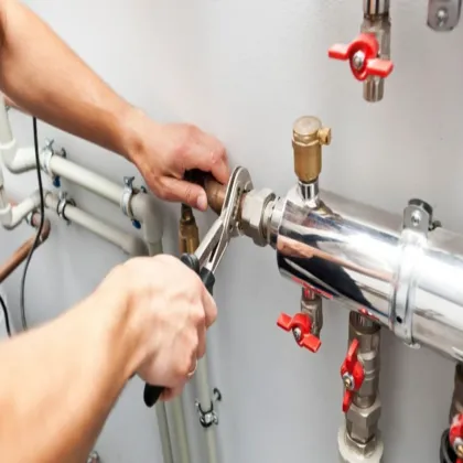 Plumber tightening a pipe fitting with a wrench on a system of pipes and valves.
