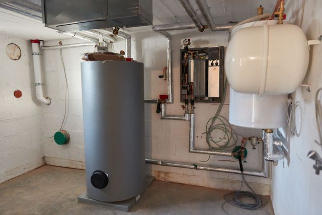 A basement with a gray water heater, white expansion tank, and connected piping.