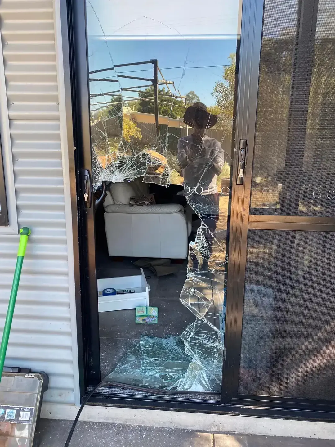 A Woman Is Standing In A Room With A Broken Glass Door — GGS Alice Glass & Aluminium In Ciccone, NT