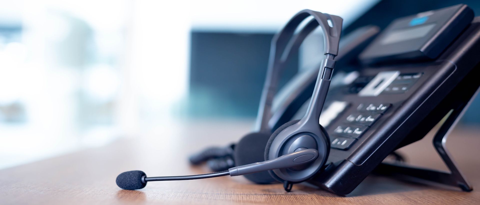 A headset is sitting next to a telephone on a desk.