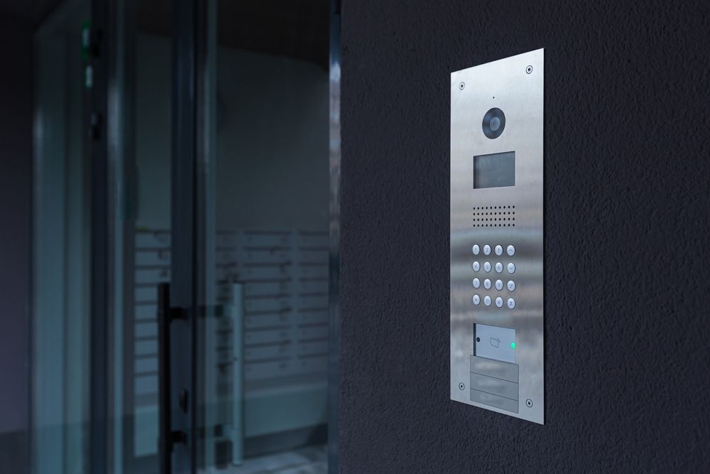 A stainless steel doorbell is hanging on a wall next to a glass door.