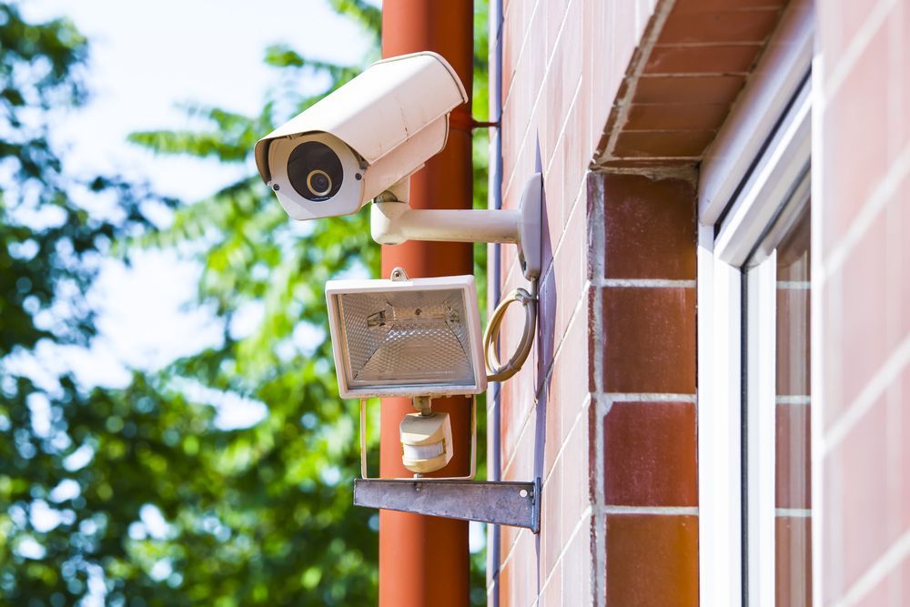 A security camera is mounted on the side of a building next to a window.