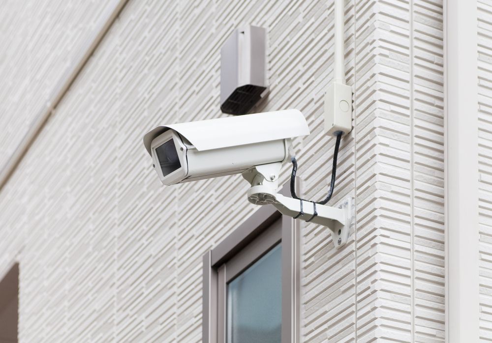 A security camera is mounted on the side of a building next to a window.