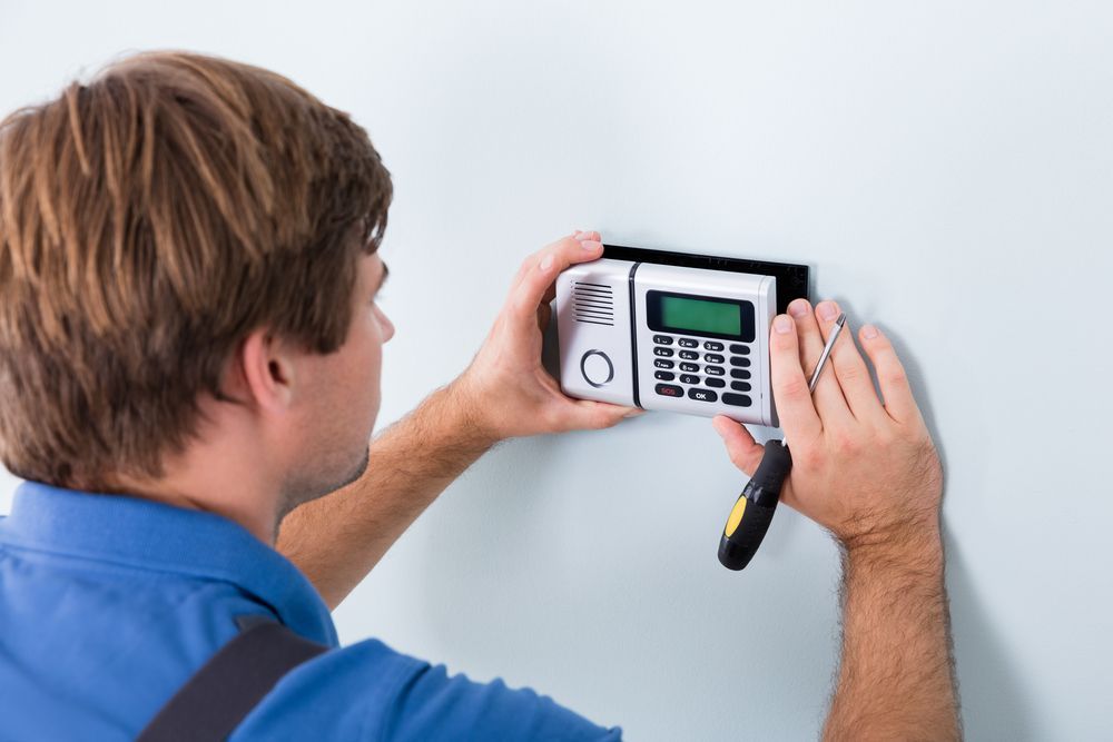 A man is installing a security system on a wall.